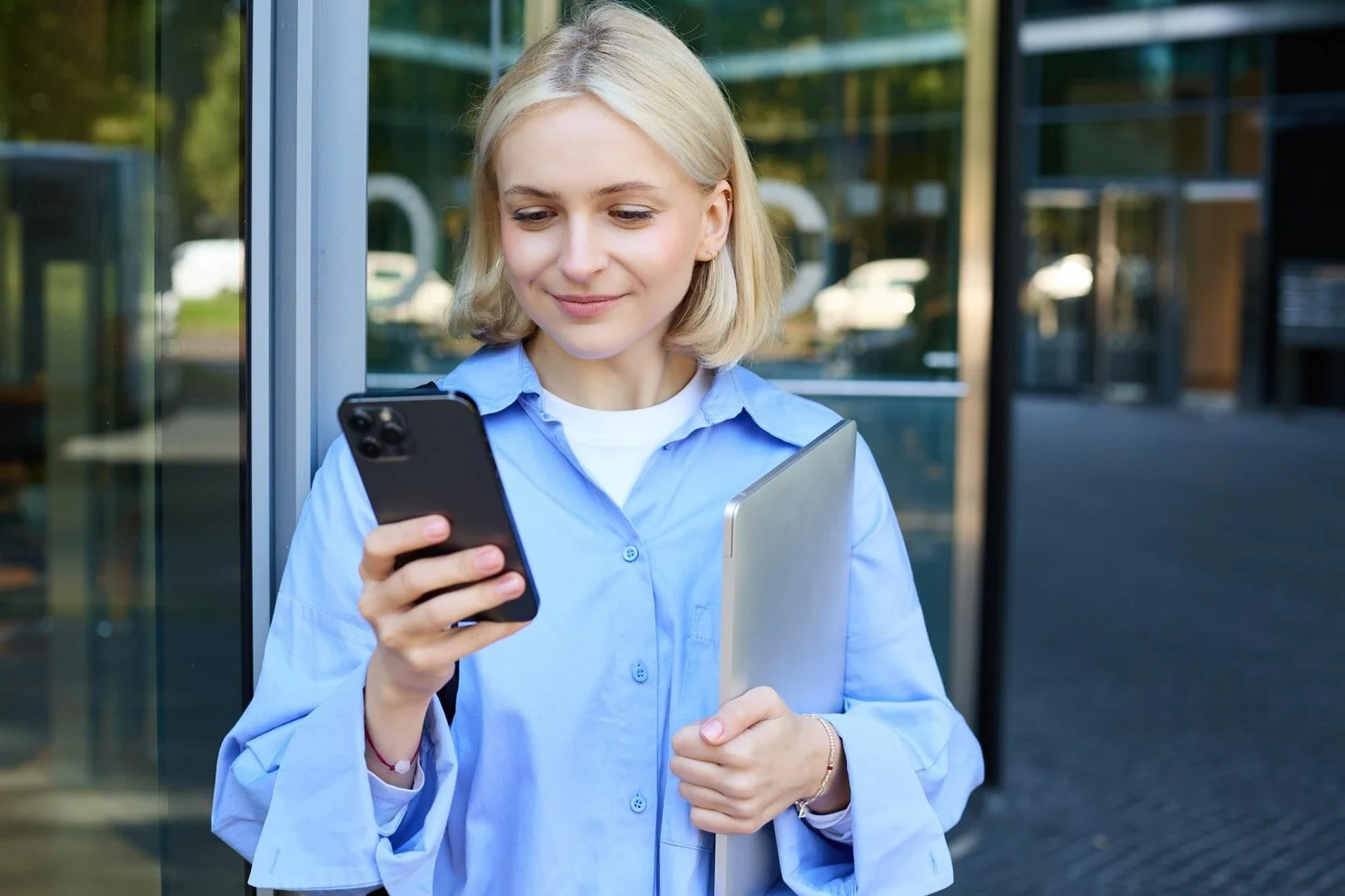 Jeune femme consultant son smartphone devant un bâtiment moderne.